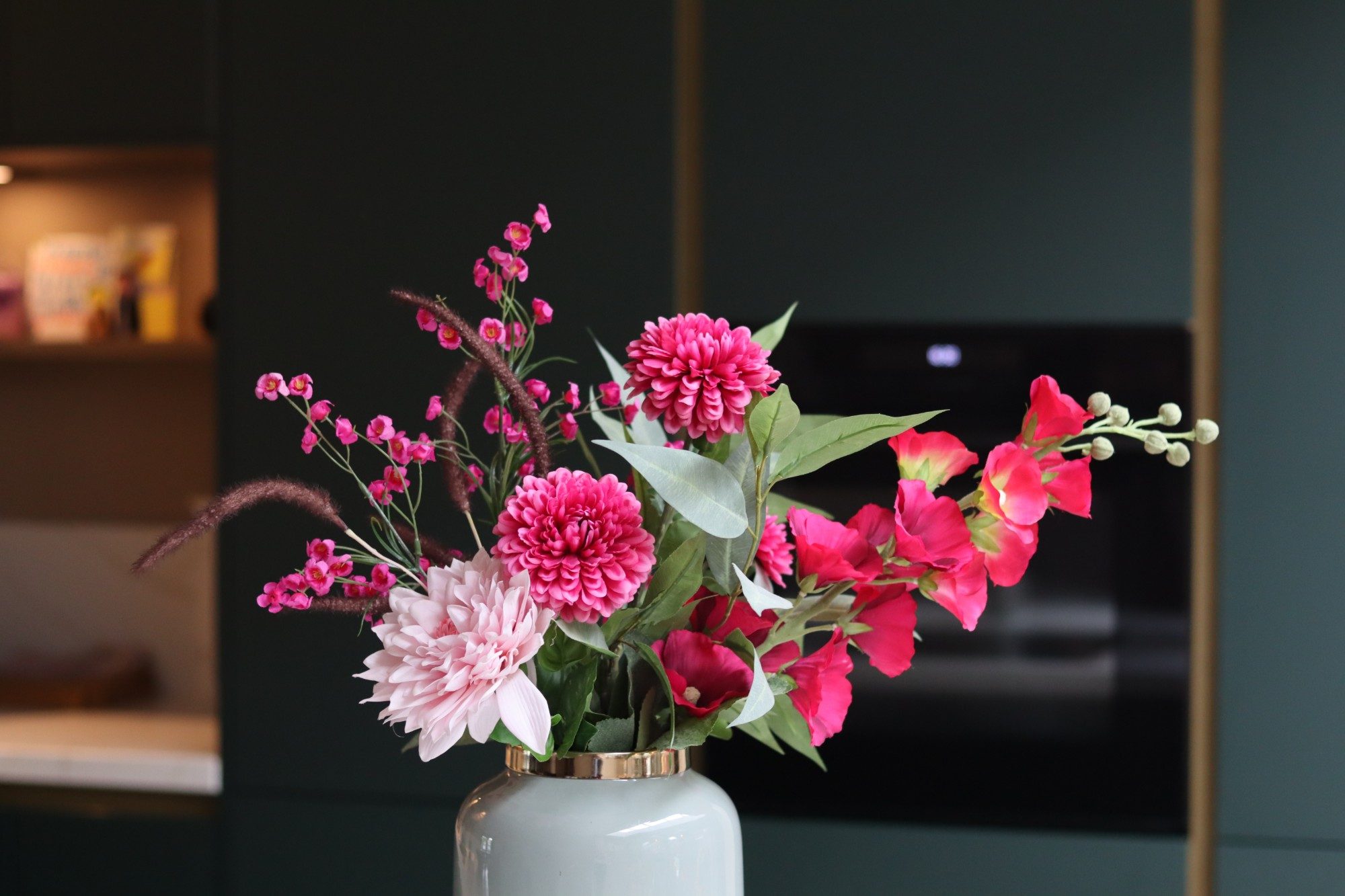 Roze boeket in een lichte vaas tegen een donkergroene keukenwand