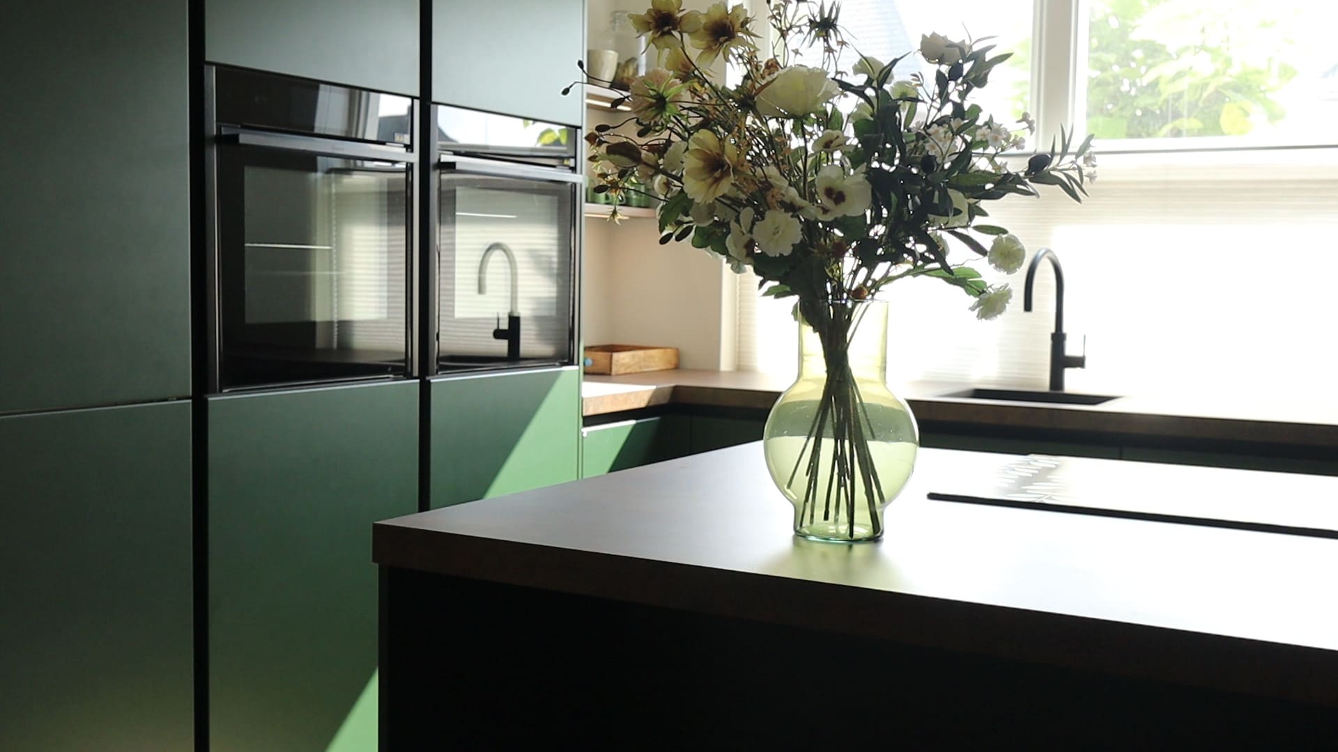 Zijden boeket op een kookeiland in een opgeleverde groene keuken