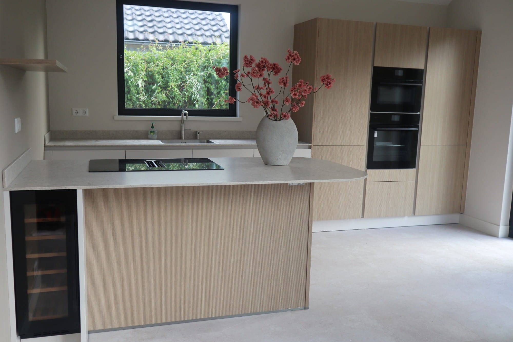 Opgeleverde keuken met houten fronten en een kookeiland, met een roze bloesemboeket in een stenen vaas