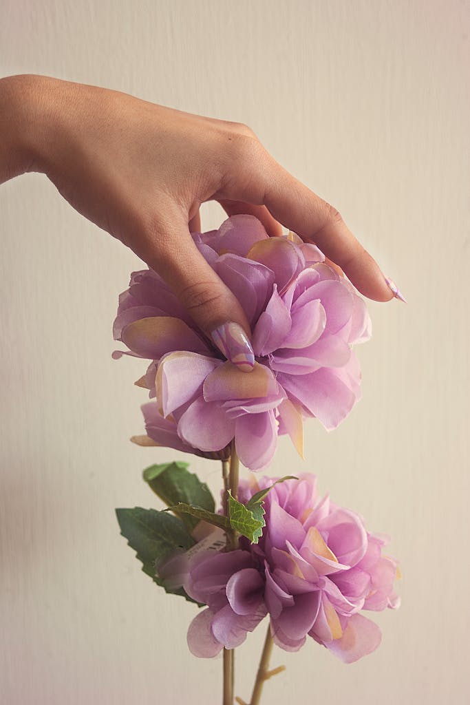 Elegant hand gently holding a lavender artificial flower against a soft background, showcasing simplicity and beauty.